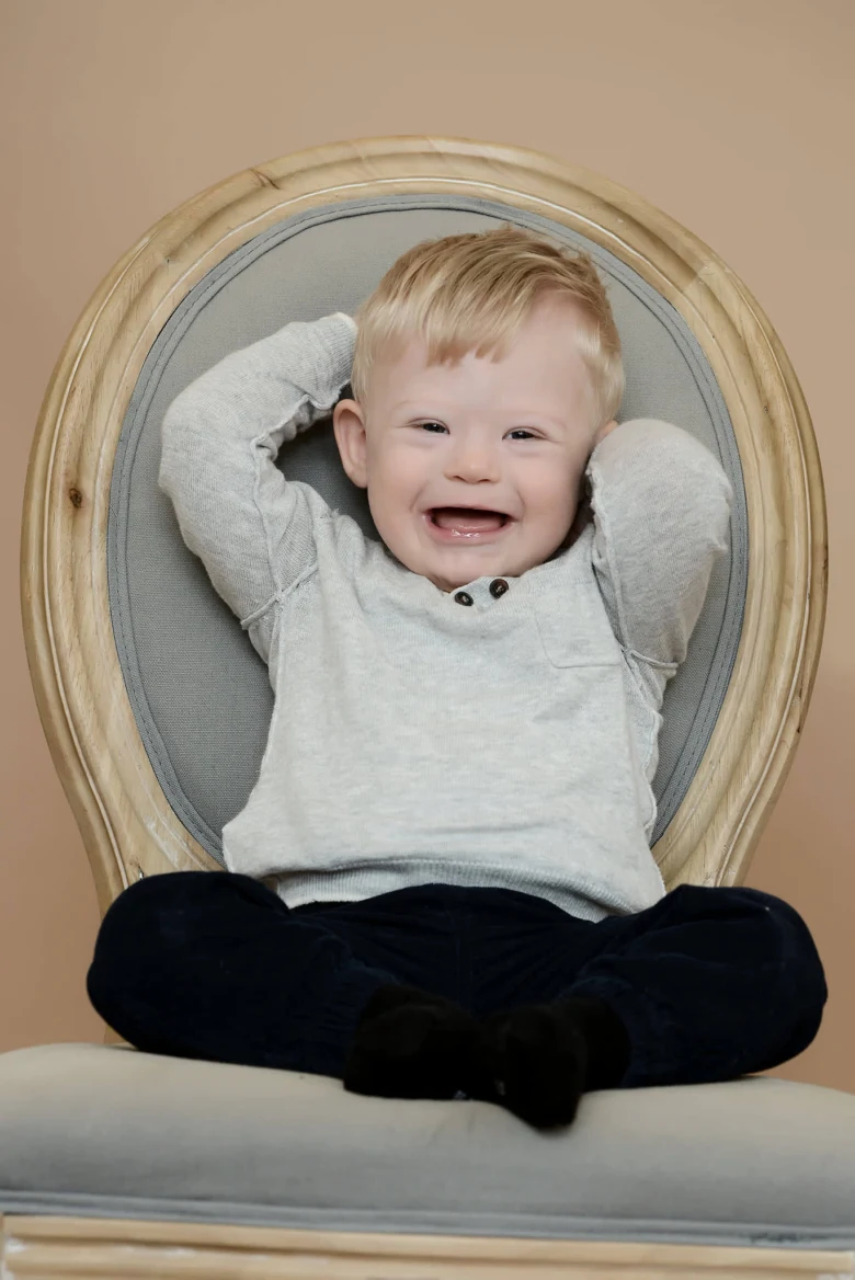 Usměvavé dítě s downovým syndromem sedí na židli.
