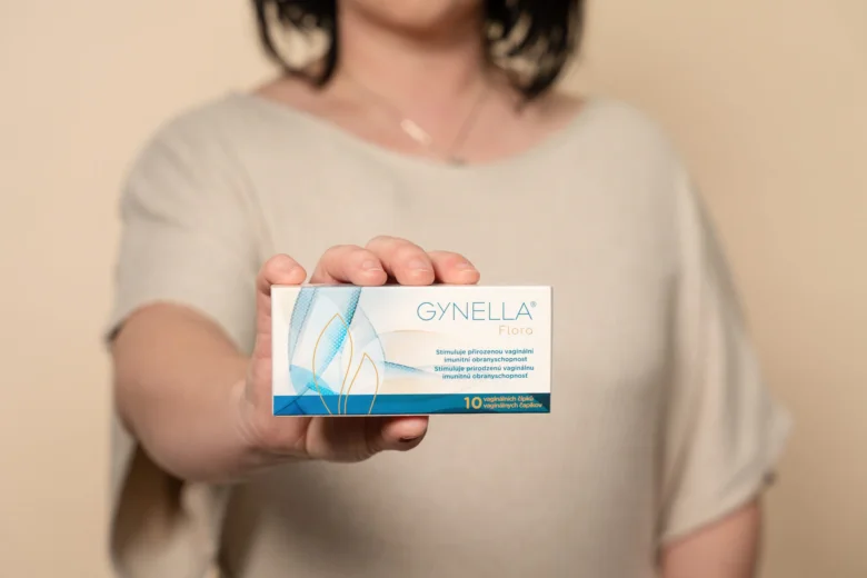 Žena drží krabičku vaginálního doplňku GYNELLA před kamerou.