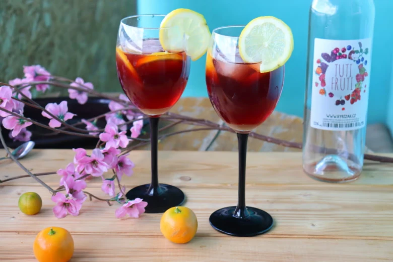 Dva sklenice s koktejlem Tutti Fruti, citrony a lahvička na dřevěném stole.
