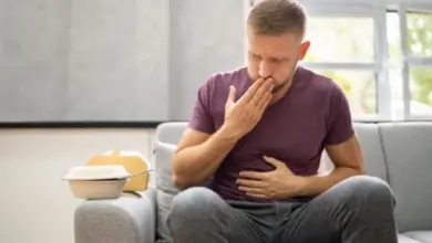 Muž sedí na gauči s bolestmi břicha po jídle.