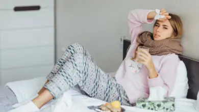 Žena leží v posteli s chřipkou a drží si nos.