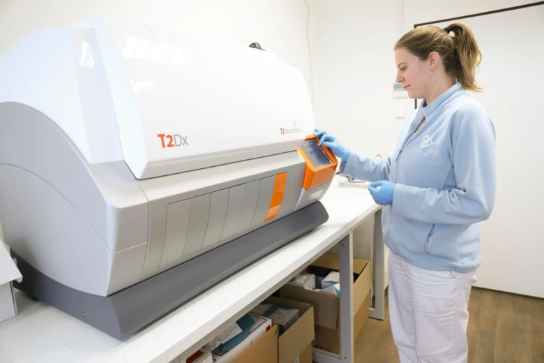 Žena v modrém oblečení ovládá diagnostický přístroj na laboratorním stole.