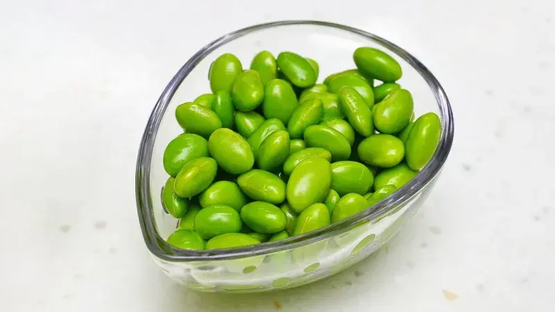 Skleněná miska plná zelených fazolí edamame na bílém povrchu.