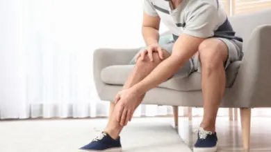 Muž sedí na gauči a drží si bolavou nohu.