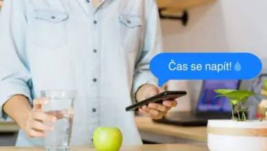 Osoba s sklenicí vody u mobilu na stole.