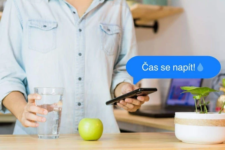 Osoba s sklenicí vody u mobilu na stole.
