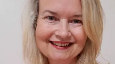 Usměvavá těhotná žena s blond vlasy v oranžovém tričku.