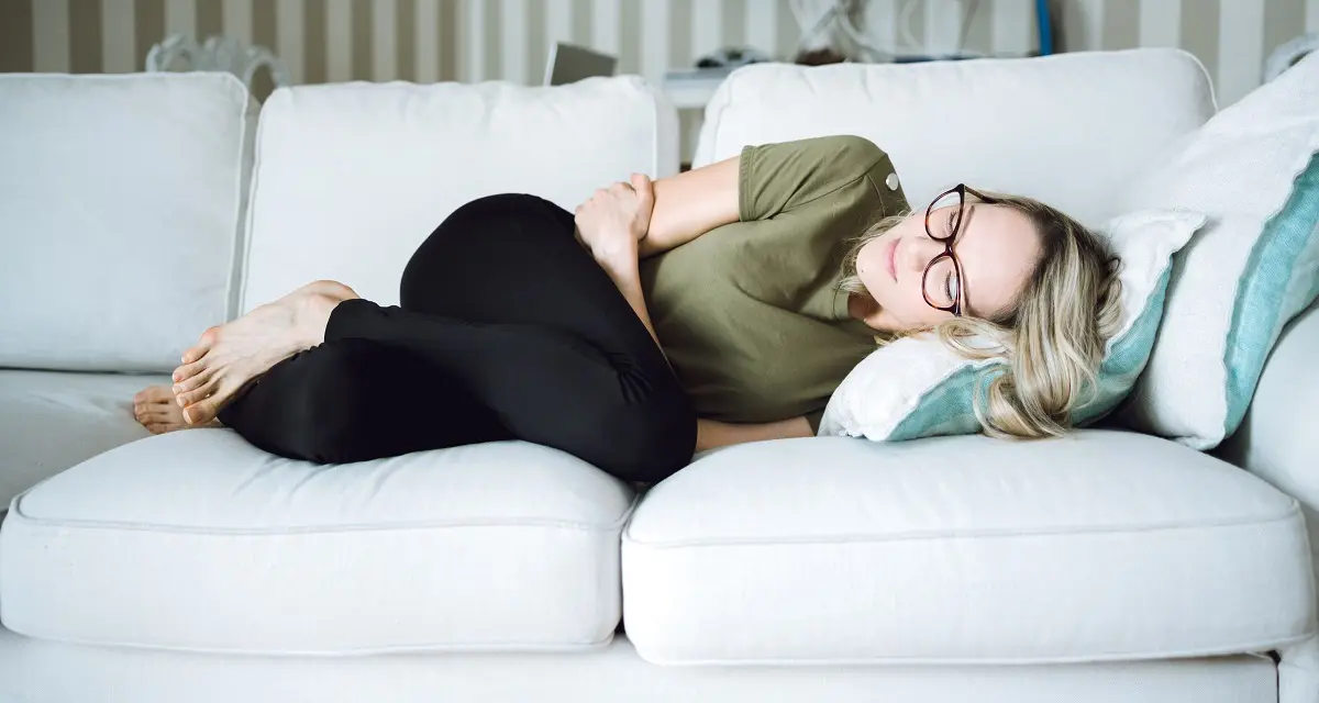 Žena leží na gauči s bolestí břicha nebo močových cest.