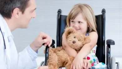 Lékař hovoří s dítětem v invalidním vozíku držícím medvěda.