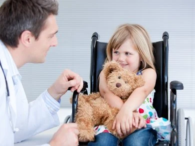 Lékař hovoří s dítětem v invalidním vozíku držícím medvěda.