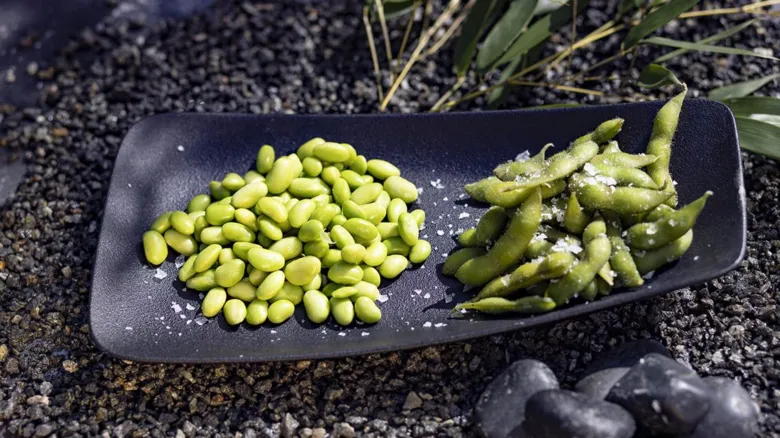 Černý talíř s vyloupanými fazolemi edamame a solenými lusky.