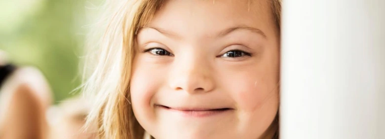 Usměvavé dítě s Downovým syndromem se dívá na kameru.