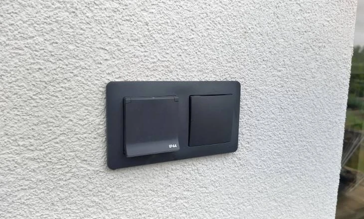 Černá dvojitá elektrická zásuvka na venkovní zdi s otevřeným krytem.