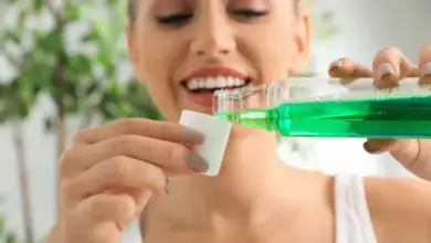 Žena nalévá zelenou ústní vodu na bavlněný tampon pro péči o ústa.