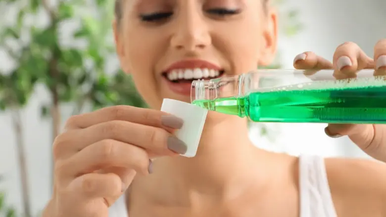 Žena nalévá zelenou ústní vodu na bavlněný tampon pro péči o ústa.