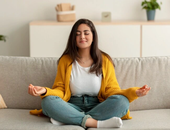 Žena sedí v lotosové poloze na gauči při meditaci.