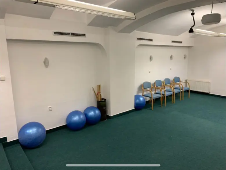 Fyzikální rehabilitační místnost s modrými cvičebními míčky a židlemi pro pacienty.