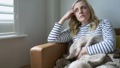 Unavená žena sedící v dečce s rukou u čela.