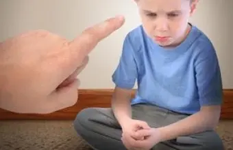 Dítě sedí na podlaze, zatímco dospělý mu ukazuje prstem.