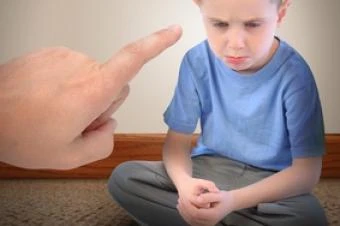 Dítě sedí na podlaze, zatímco dospělý mu ukazuje prstem.