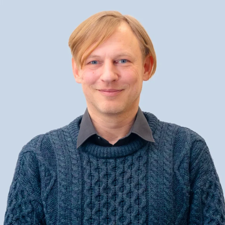 Muž v modrém svetrku na neutrálním pozadí.