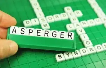 Ruka drží kostičky s nápisem Asperger nad křížovkou.