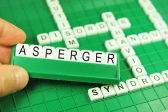 Ruka drží kostičky s nápisem Asperger nad křížovkou.