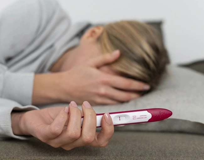 Žena drží pozitivní těhotenský test v ruce.