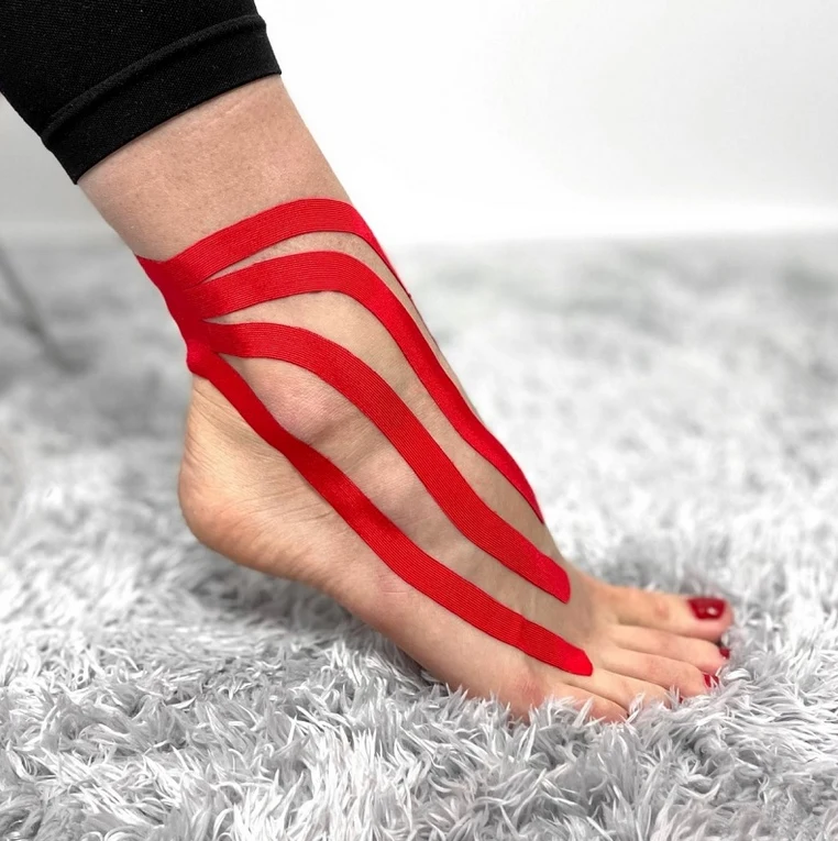 Červená kinéziotape na kotníku pro podporu při výronu.