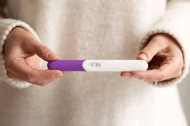 Žena drží v rukou pozitivní těhotenský test s dvěma čarami.