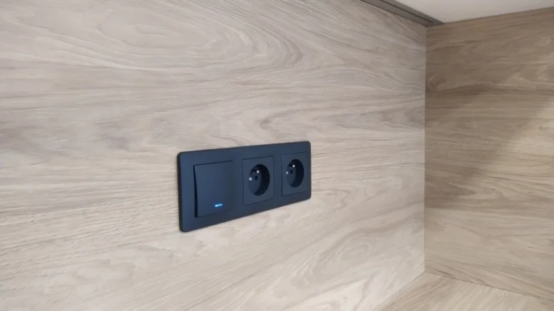 Černý elektrický panel s vypínačem a zásuvkou na dřevěné stěně.