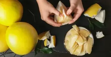 Ruční loupaní žlutého pomeranče s viditelnými plátky.