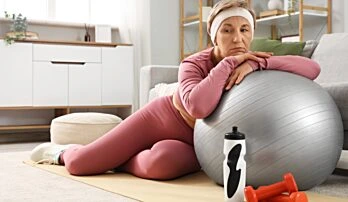 Žena v sportovním oblečení odpočívá na fitbalu s činkami.