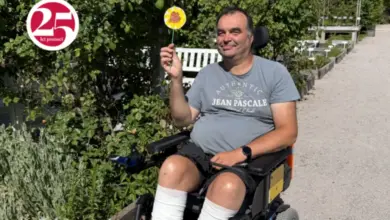 Muž v invalidním vozíku drží žlutý květ venku.
