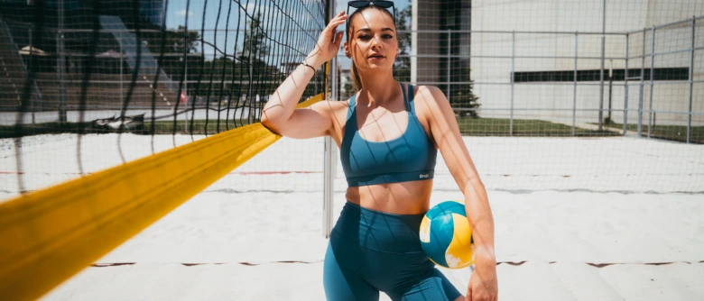 Žena v sportovním oblečení s volejbalem na plážovém dvorku.