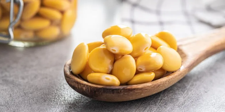 Dřevěná lžíce plná žlutých fazolí edamame na šedém povrchu.