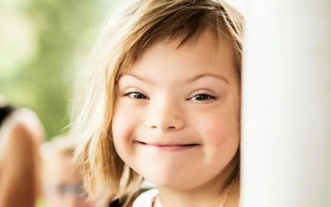 Usměvavé dítě s downovým syndromem se dívá zpoza předmětu.