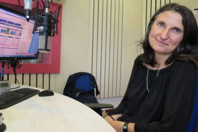 Žena v rozhlasové studii s mikrofony u počítače.