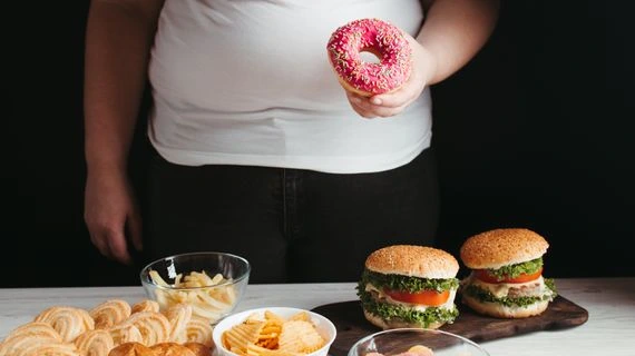 Osoba drží rohlík s cukrem vedle burgerů a bramborových lupínků.