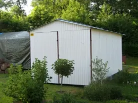 Bílá zahradní stodola v zeleném okolí s rostlinami.