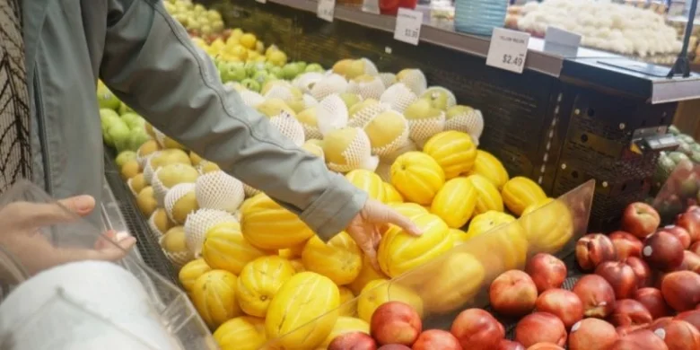 Ruce vybírají žluté ovoce z košíku v obchodě s potravinami.